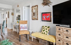 A living room with a television, a framed cityscape picture, a chair, a small table, and a decorative mirror.