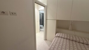 Ein Schlafzimmer mit Bett, Kleiderschrank und einem durchgehenden Türrahmen sichtbarem Badezimmer.
