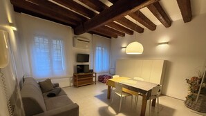Ein Wohnzimmer mit Sofa, Fernseher, Esstisch mit Stühlen und einer Decke mit freiliegenden Balken.