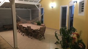 A covered patio area with a wooden table and chairs, surrounded by potted plants.