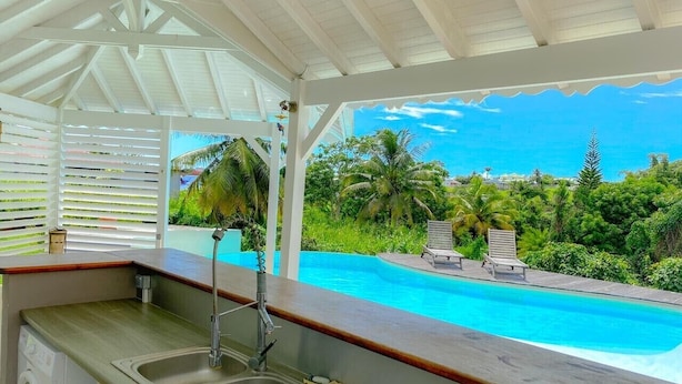 A kitchen with a view of a pool and lounge chairs.