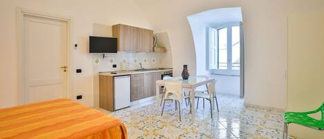 Ein kleines Zimmer mit Bett, Küchenzeile, Essbereich und Fenster.