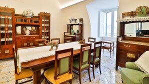 A dining room with a wooden table, chairs, and a lace tablecloth. There are wooden cabinets with glass doors and a mirror on the wall. - Della Monica Rooms (Vietri sul Mare)