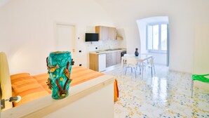 A modern room with a bed, a small table, a chair, a kitchen area, and a dining table with chairs. - Della Monica Rooms (Vietri sul Mare)