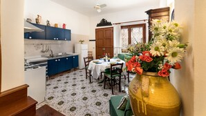 Een keuken met blauwe kastjes, een eettafel gedekt voor vier personen, en een vaas met bloemen op de tafel.