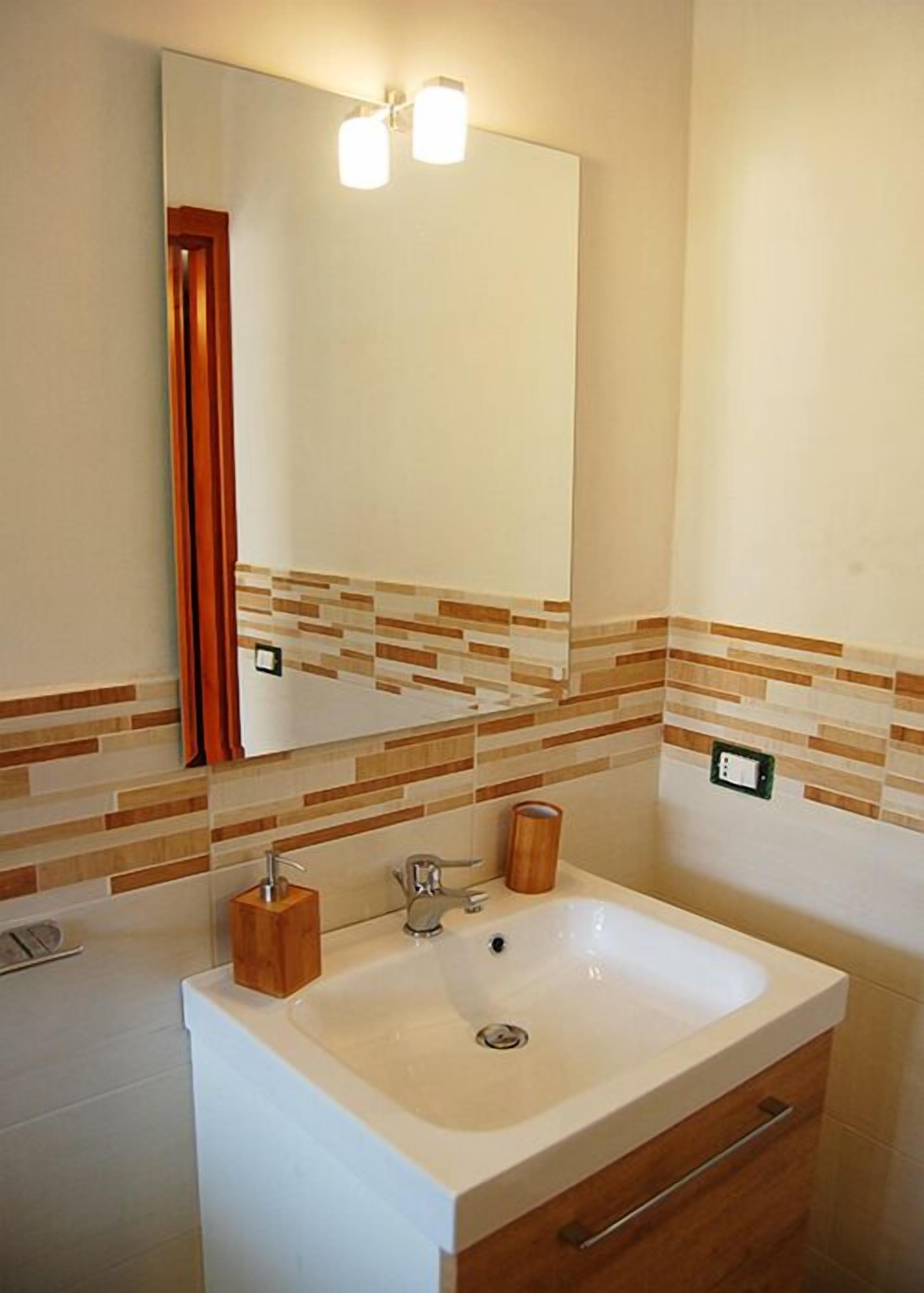 Ein Badezimmer mit einem weißen Waschbecken, einem Holzschrank und einem Spiegel mit zwei Lampen.