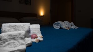 A neatly made bed with a blue bedspread, white towels, and rolled towels on the side.