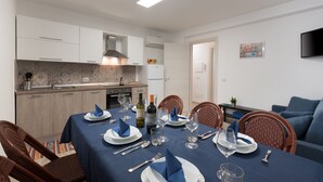 A dining area with a table set for four, a kitchen in the background, and a television mounted on the wall.