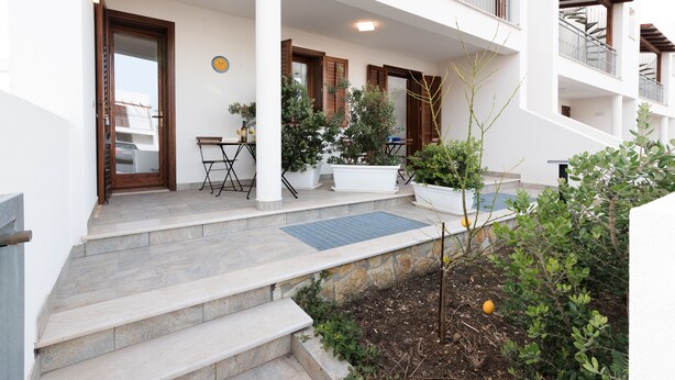 A residential building with a covered porch, outdoor seating, potted plants, and a small garden area.