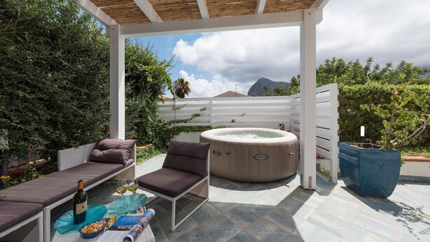 Un espace extérieur abrité, aménagé avec un coin salon, un jacuzzi, des chaises longues et une table où sont servis des collations et des boissons.