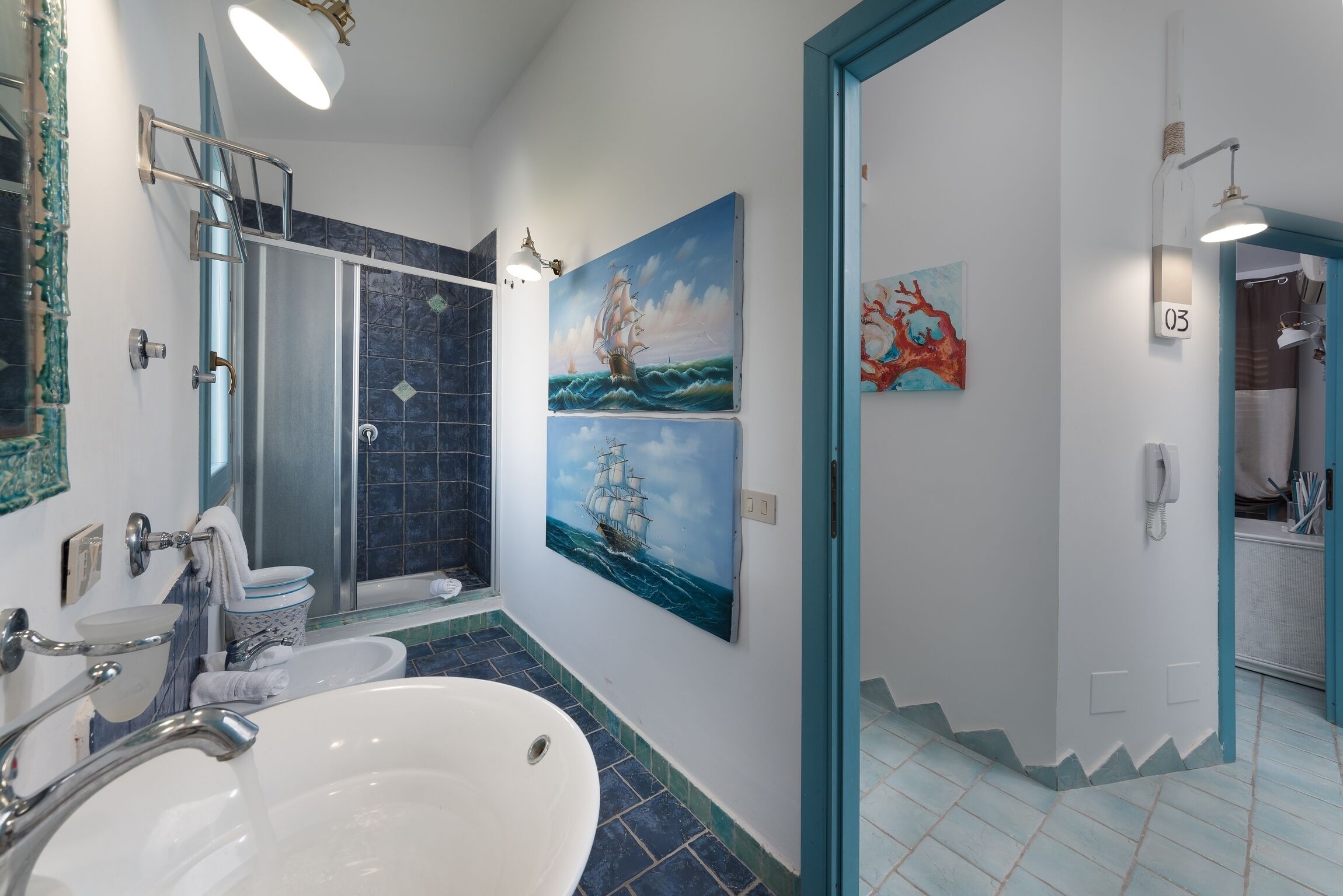 A bathroom with a large bathtub, a shower, and a toilet. There are two paintings on the wall and a number '03' sign.
