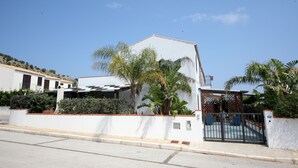 Une maison moderne avec une façade blanche, une entrée sécurisée par un portail et un petit patio aménagé avec du mobilier d’extérieur.