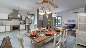 Une cuisine moderne avec des meubles blancs, une table à manger en bois pour six personnes et une grande fenêtre.