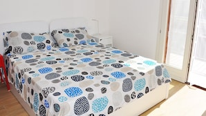 Une chambre à coucher avec un lit recouvert d’une couvre-lit à motifs, une table de chevet blanche et une fenêtre avec des stores.