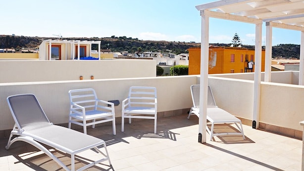 Une terrasse sur le toit, avec des chaises et une table en métal blanc, une pergola et une vue sur les bâtiments en arrière-plan.