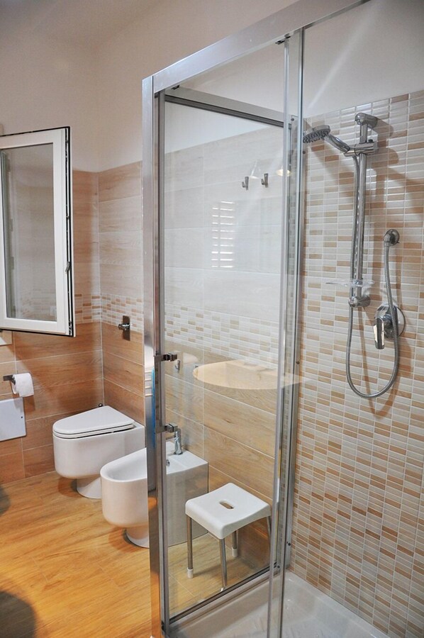 Une salle de bain moderne avec une douche à parois de verre, des toilettes, des bidet et un petit tabouret.