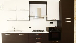 Una cocina moderna con un lavamanos de acero inoxidable, estufa a gas, horno empotrado y armarios oscuros con tiradores metálicos.