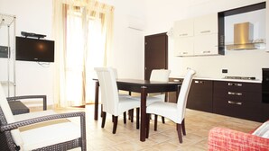 Un comedor con una mesa y sillas, un televisor montado en la pared y una zona de cocina con armarios y un microondas.
