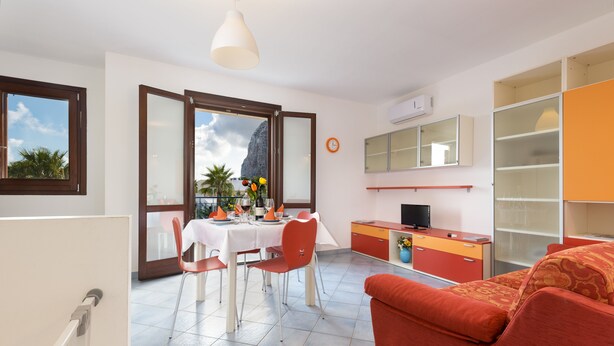 A modern apartment with a dining area, a sofa, a TV, and a view of the mountains. - I tre Golfi Zenzero (San Vito Lo Capo)