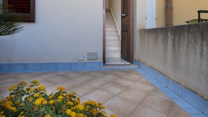 A building with a staircase leading to an upper floor, a light fixture above the door, and a concrete wall with a pipe. - I tre Golfi Zenzero (San Vito Lo Capo)