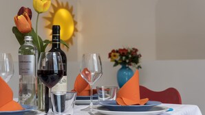 A table set with plates, glasses, and bottles, with a vase of flowers and a sun in the background. - I tre Golfi Zenzero (San Vito Lo Capo)
