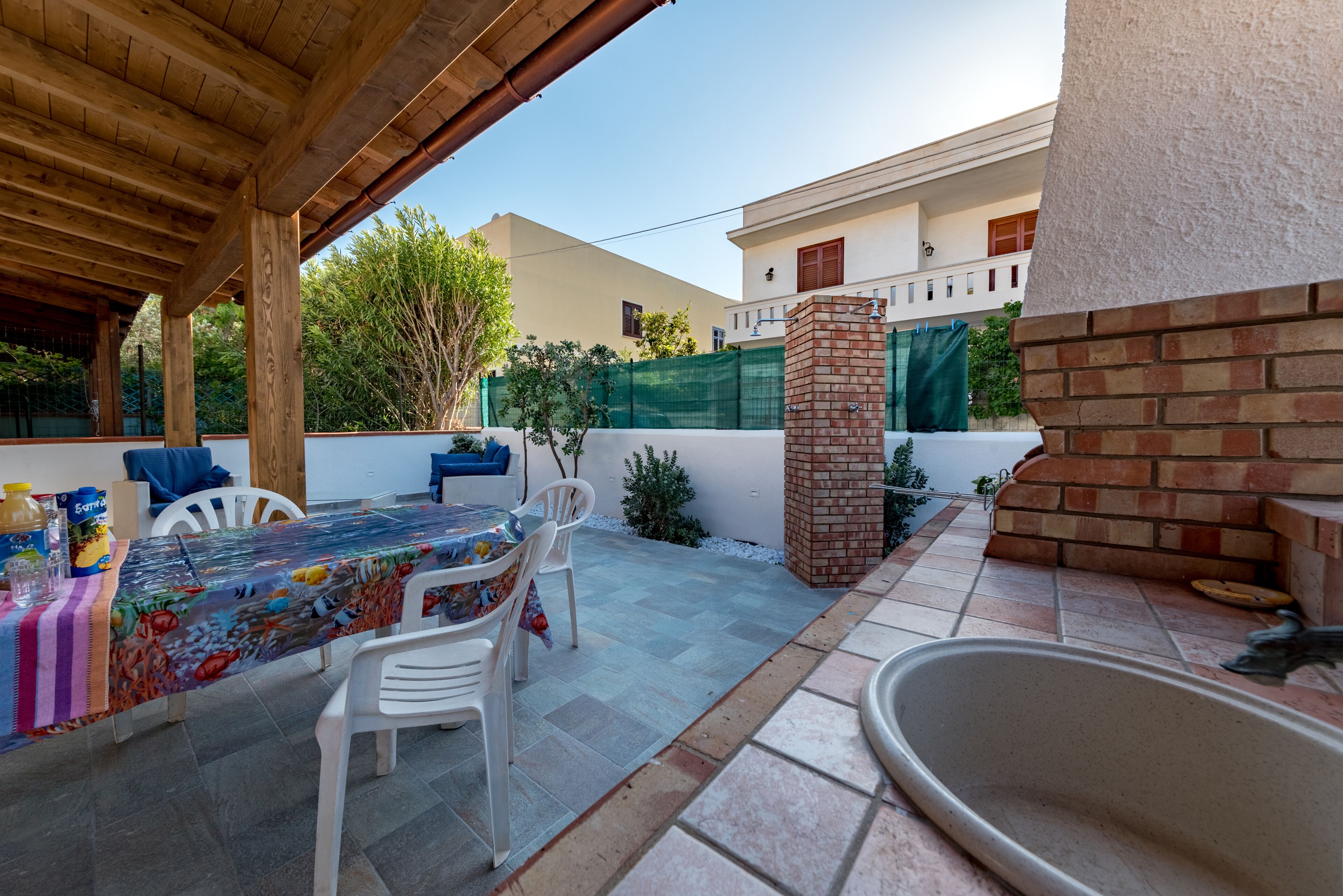 Une terrasse extérieure dotée d’un espace salon couvert, d’un four en briques et d’un sol carrelé.