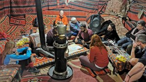A group of people seated around a central table in a room with patterned rugs and traditional decor.