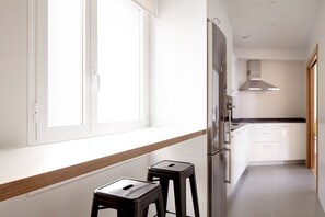 Una cocina moderna con armarios blancos, un refrigerador de acero inoxidable y dos taburetes.