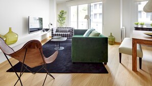 A modern living room with a green sofa, a black and white checkered sofa, a wooden dining table, and a black rug. - Muinoa 1 by FeelFreeRentals (Donostia)