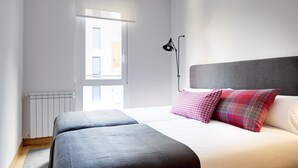 A bedroom with a bed, two bedside tables, a window, and a radiator. - Muinoa 1 by FeelFreeRentals (Donostia)