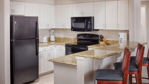 A kitchen with white cabinets, a black refrigerator, a microwave, a stove, and a granite countertop.