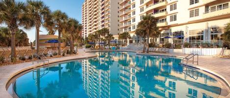A swimming pool with a clear blue water, surrounded by palm trees and a tall building in the background.