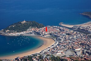 An aerial view of a coastal city with a prominent hill, a beach, and a dense urban area with buildings and a bridge.