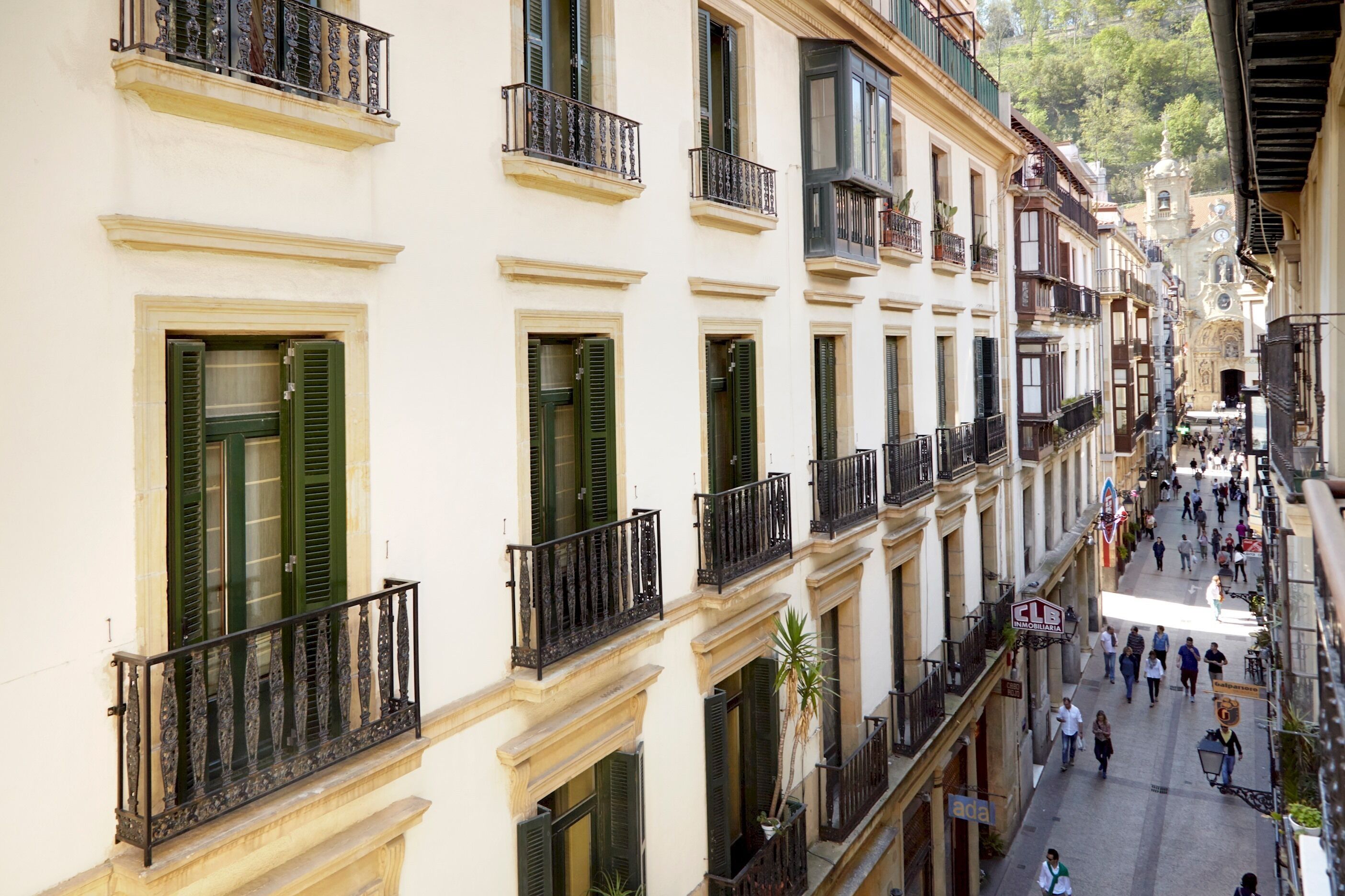 A multi-story building with balconies, a pedestrian street, and a church in the background.