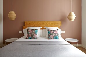 A neatly made bed with a wooden headboard, two pillows with floral patterns, and two hanging wooden light fixtures.