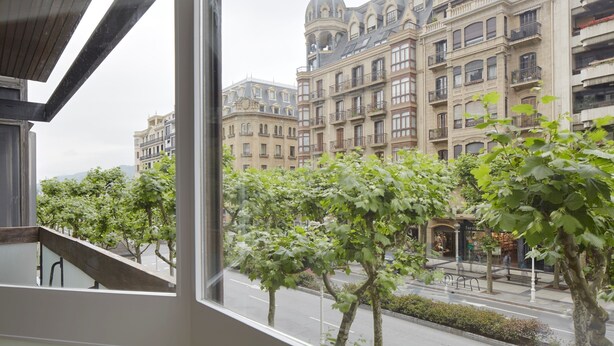 A view from a window overlooking a street with historic buildings, trees, and a clear sky. - Enbata by FeelFreeRentals (San Sebastian)
