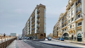 A multi-story building with balconies and a pedestrian walkway alongside a road with parked cars. - Príncipe by FeelFreeRentals (Donostia)