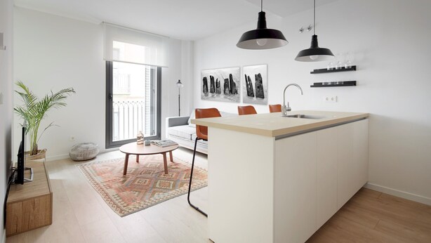 Cozinha moderna com ilha central, iluminação pendente e área de jantar com sofá e mesa de centro.