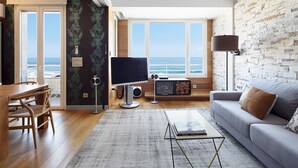 A modern living room with a large window overlooking the ocean, a flat-screen TV, a sofa, and a dining area with wooden furniture. - Kantauri by FeelFreeRentals (Donostia)