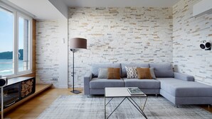A modern living room with a grey sofa, a coffee table, a floor lamp, and a view of the sea through large windows. - Kantauri by FeelFreeRentals (Donostia)