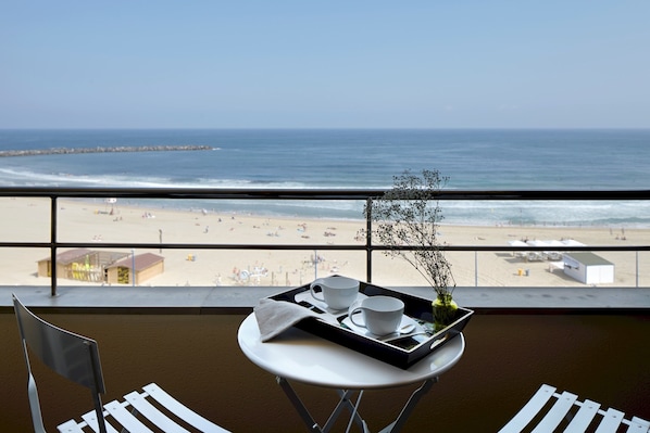 A balcony with a table set for two, overlooking a beach with a pier in the distance.