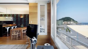 A modern living room with a large TV, wooden furniture, and a view of a beach and cityscape. - Kantauri by FeelFreeRentals (Donostia)