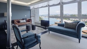 Ein modernes Wohnzimmer mit einem großen Fenster, einem blauen Sofa, einem braunen Ledersofa und einem blauen Sessel.