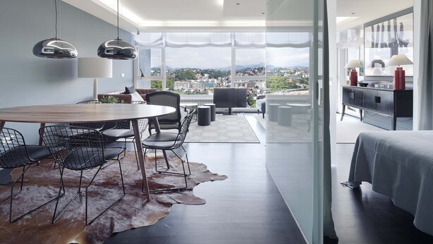 Ein modernes Hotelzimmer mit Essbereich, einem großen Fenster mit Blick auf die Stadt, einem Bett und einem Badezimmer.