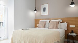 Un lit bien fait, agrémenté d’oreillers à rayures, d’un plaid beige et d’un tableau encadré accroché au mur.