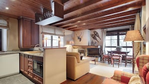 A cozy living area with a fireplace, wooden ceiling, and a dining table with chairs. - Val de Ruda Luxe 65 by FeelFree Rentals (Baqueira)