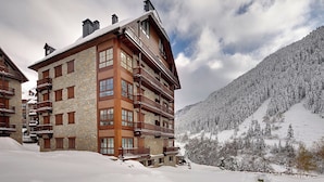 A multi-story wooden building with balconies, set against a snowy mountain backdrop. - Val de Ruda Luxe 65 by FeelFree Rentals (Baqueira)