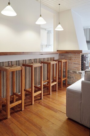 A bar area with wooden stools, a brick wall, and hanging pendant lights. - Comets by FeelFree Rentals (Vielha e Mijaran)