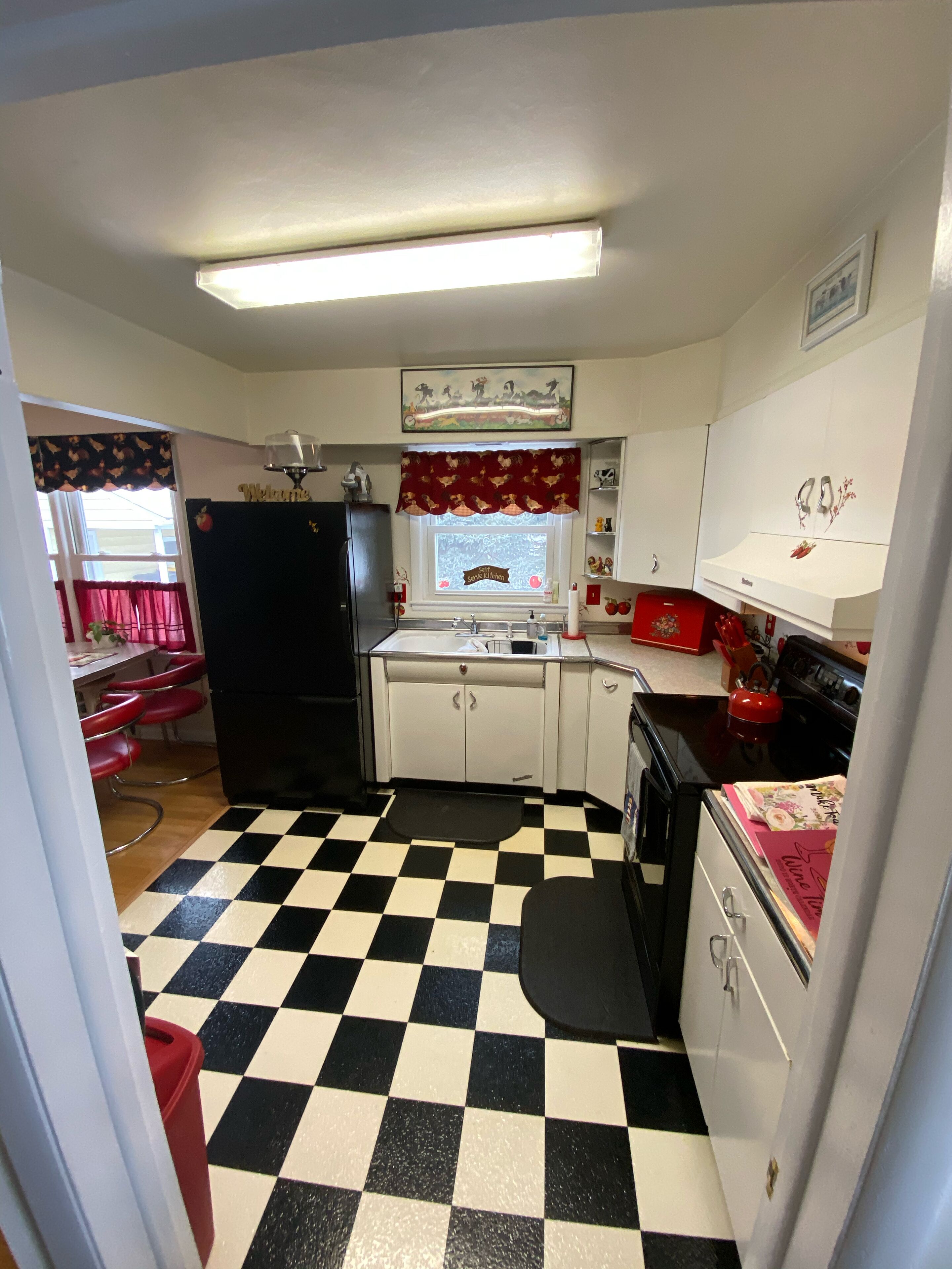 Una cocina pequeña con suelo blanco y negro a cuadros, un refrigerador, una estufa y un lavamanos.