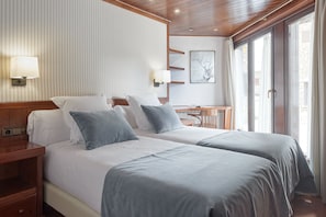 A hotel room with a large bed, two bedside tables, a desk, and a window with curtains.